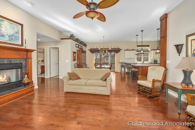 living room with wood finished floors, a fireplace, and ceiling fan with notable chandelier