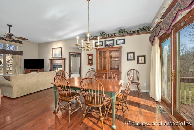 dining area featuring visible vents, wood finished floors, a tiled fireplace, and ceiling fan with notable chandelier