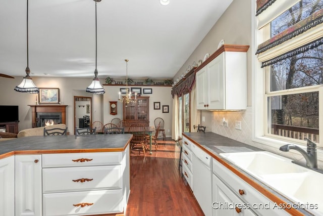 kitchen with dark countertops, dark wood-style floors, a warm lit fireplace, and a sink