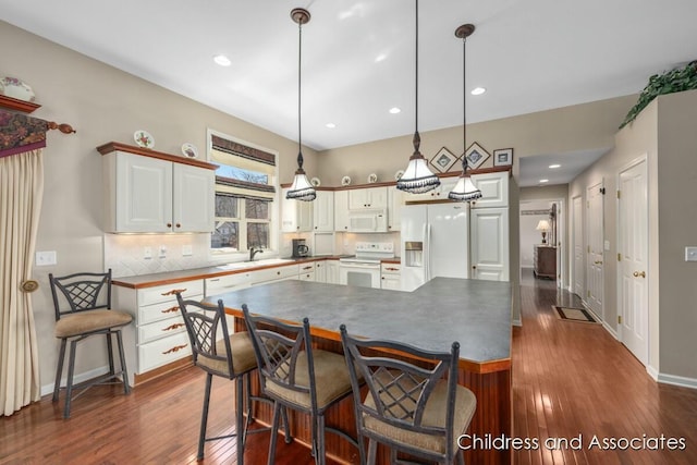 kitchen with white appliances, dark wood finished floors, decorative backsplash, white cabinets, and decorative light fixtures