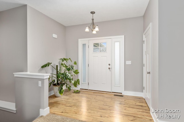 entryway with light wood finished floors, a chandelier, visible vents, and baseboards