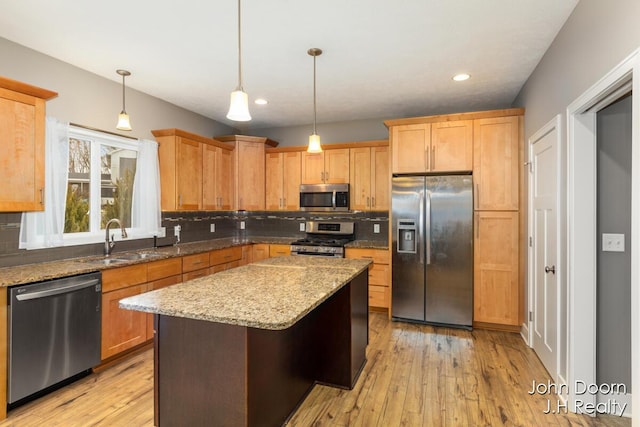 kitchen with a sink, decorative backsplash, appliances with stainless steel finishes, light wood-type flooring, and a center island