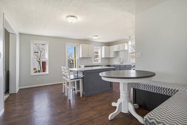 kitchen with a breakfast bar, a sink, a center island, white cabinetry, and dark wood-style flooring