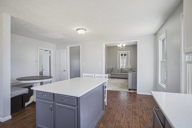 kitchen with gray cabinets, light stone counters, a center island, baseboards, and dark wood-style flooring