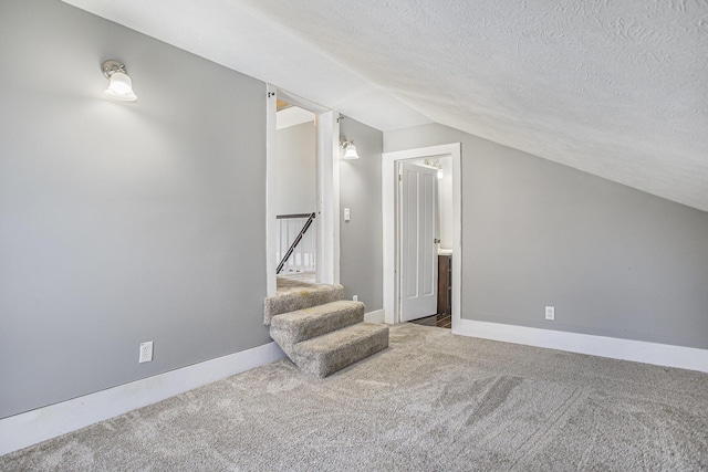 additional living space with baseboards, carpet, stairway, lofted ceiling, and a textured ceiling