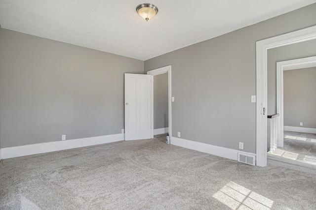 carpeted spare room with baseboards, visible vents, and a textured ceiling