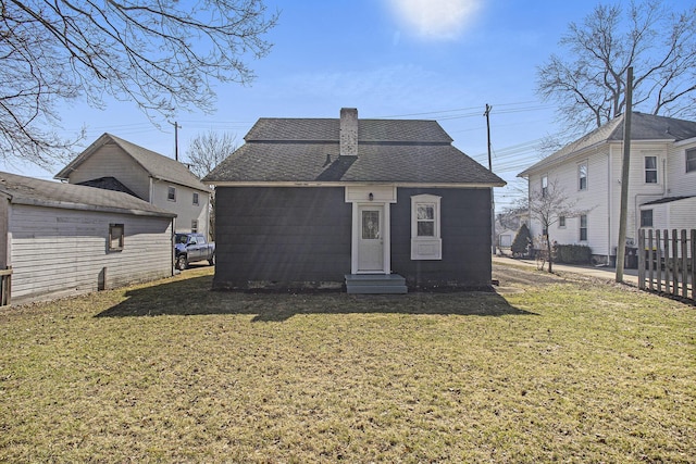 back of house featuring a lawn, entry steps, fence, a shingled roof, and a chimney