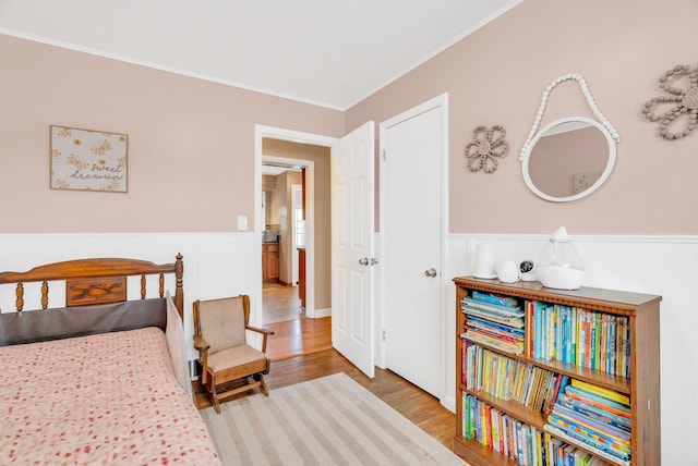 bedroom featuring wainscoting, crown molding, and light wood-style flooring