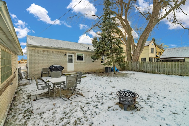 snow covered property featuring cooling unit, brick siding, an outdoor fire pit, and fence