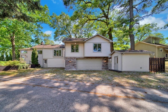 view of front facade featuring fence, driveway, an outdoor structure, a garage, and stone siding