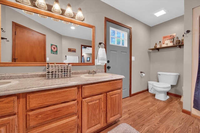 full bathroom with toilet, a sink, wood finished floors, double vanity, and baseboards