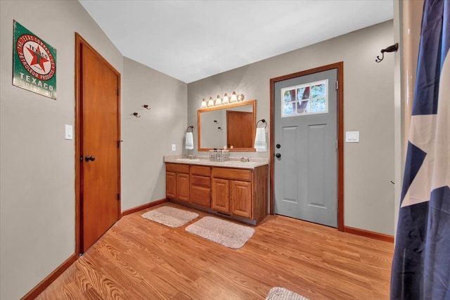 full bathroom with double vanity, a sink, baseboards, and wood finished floors