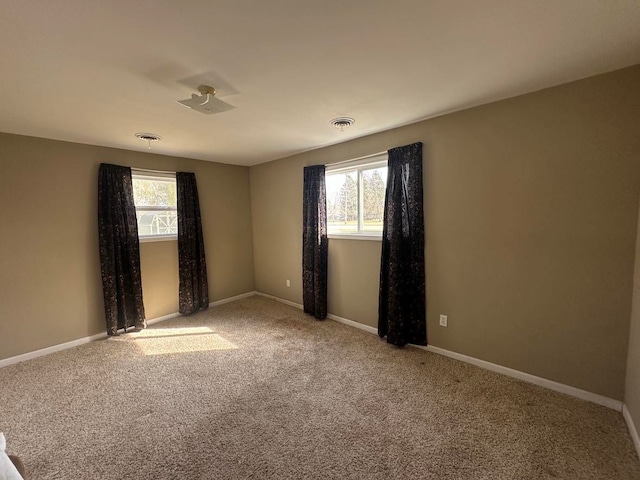 carpeted empty room featuring baseboards, visible vents, and a wealth of natural light