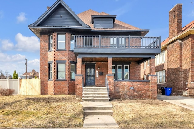 view of front of property with brick siding, a balcony, and fence