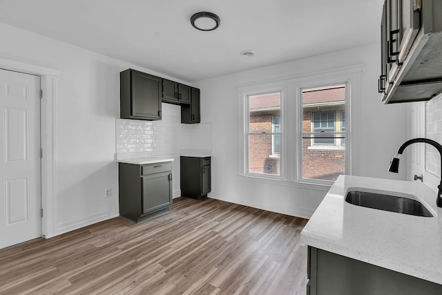 kitchen featuring light stone countertops, visible vents, light wood finished floors, a sink, and decorative backsplash