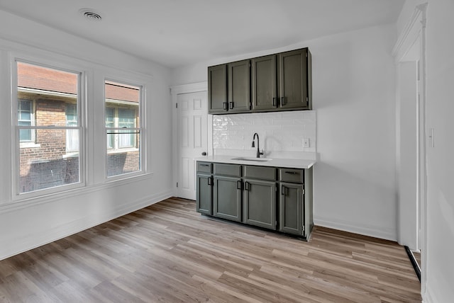 kitchen with light wood finished floors, visible vents, backsplash, light countertops, and a sink