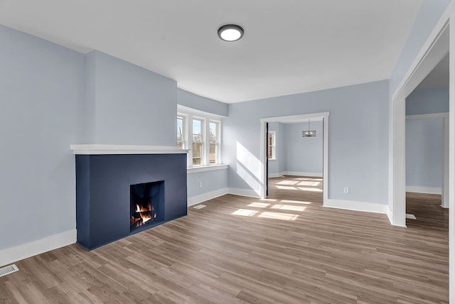 unfurnished living room with visible vents, wood finished floors, baseboards, and a lit fireplace