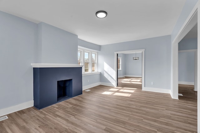 unfurnished living room with visible vents, a fireplace, baseboards, and wood finished floors