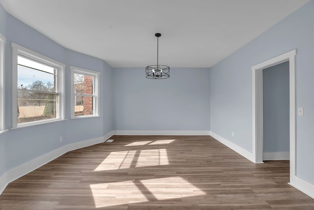 unfurnished room with baseboards, a notable chandelier, and wood finished floors