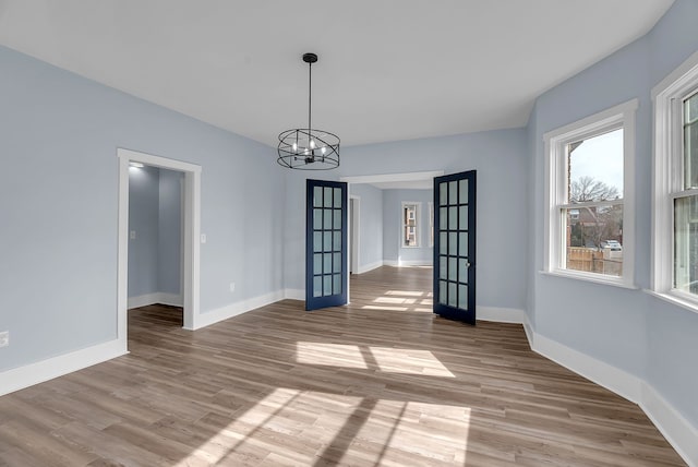 empty room with french doors, baseboards, a notable chandelier, and wood finished floors