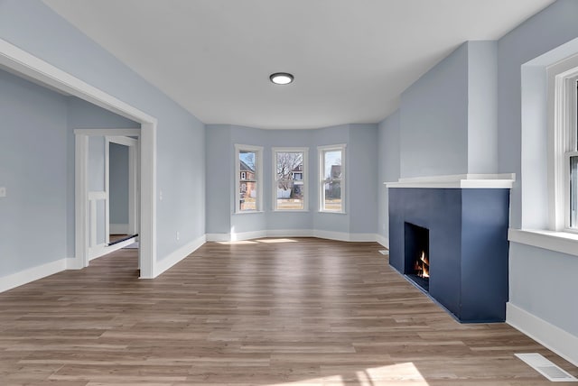 unfurnished living room featuring visible vents, wood finished floors, baseboards, and a warm lit fireplace