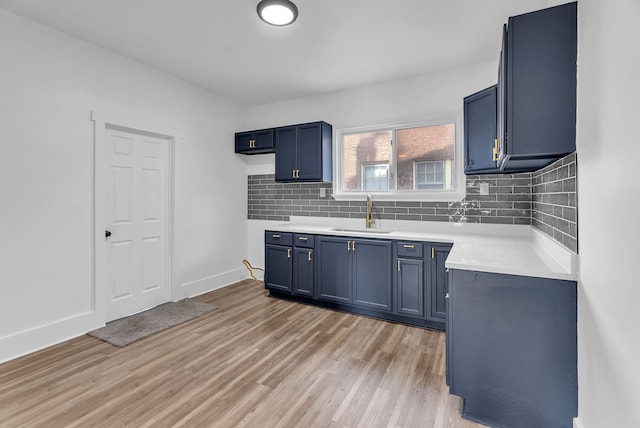 kitchen with light wood finished floors, a sink, blue cabinetry, tasteful backsplash, and light countertops