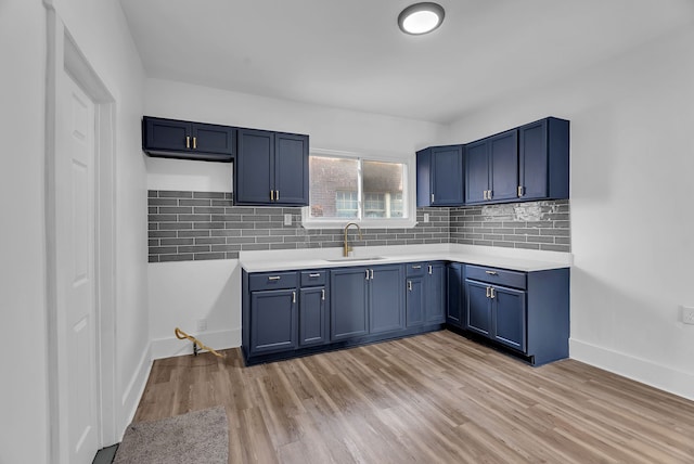 kitchen featuring tasteful backsplash, blue cabinetry, light countertops, light wood-type flooring, and a sink