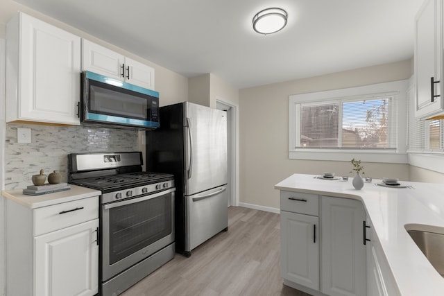 kitchen featuring light wood-style flooring, light countertops, appliances with stainless steel finishes, white cabinetry, and tasteful backsplash