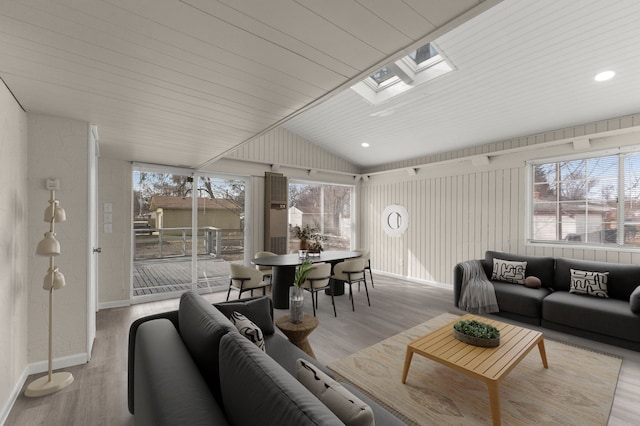 living room with vaulted ceiling with skylight, wood finished floors, baseboards, and a wealth of natural light