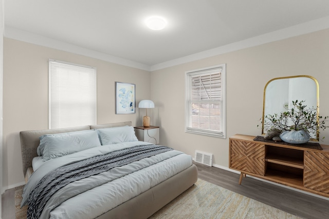 bedroom featuring visible vents, baseboards, wood finished floors, and crown molding