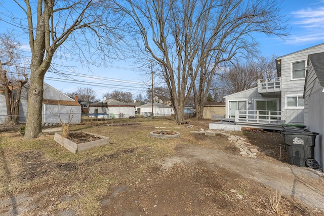 view of yard featuring a trampoline, fence, a wooden deck, an outdoor fire pit, and a balcony