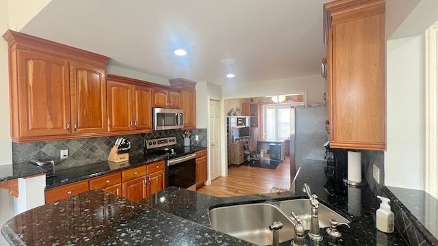 kitchen featuring a sink, stainless steel appliances, dark stone countertops, and decorative backsplash