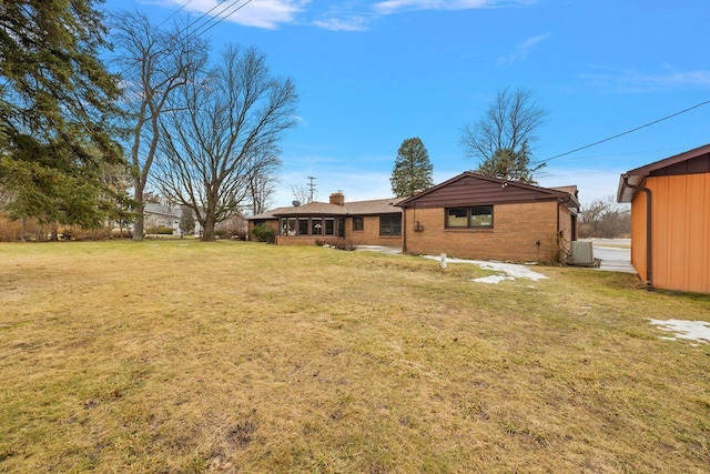 exterior space with brick siding, central AC unit, a chimney, and a lawn