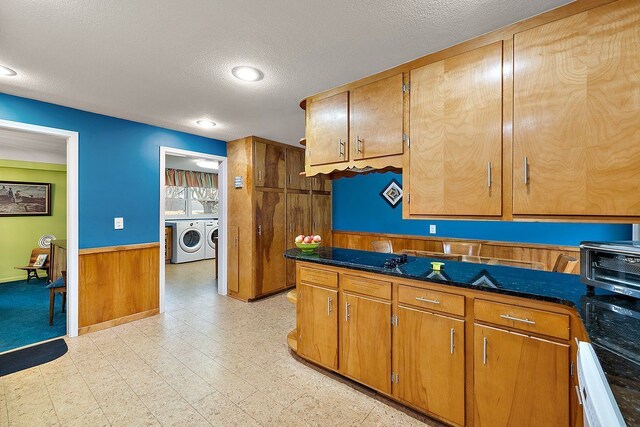 kitchen featuring independent washer and dryer, a textured ceiling, wooden walls, wainscoting, and light floors