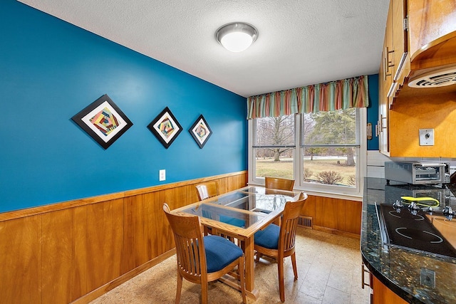 dining room featuring wooden walls, visible vents, a toaster, wainscoting, and a textured ceiling