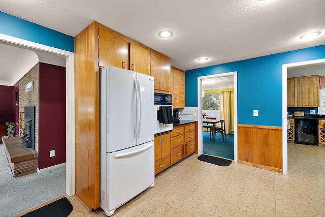 kitchen with brown cabinetry, light floors, freestanding refrigerator, wall oven, and wainscoting