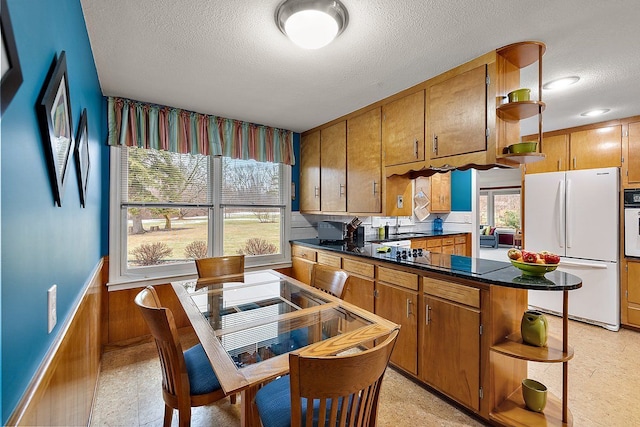 kitchen with open shelves, dark countertops, a textured ceiling, white appliances, and brown cabinetry