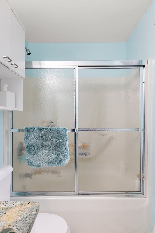 bathroom featuring combined bath / shower with glass door and toilet