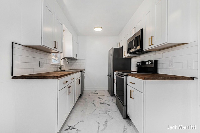 kitchen featuring marble finish floor, butcher block countertops, a sink, stainless steel appliances, and decorative backsplash