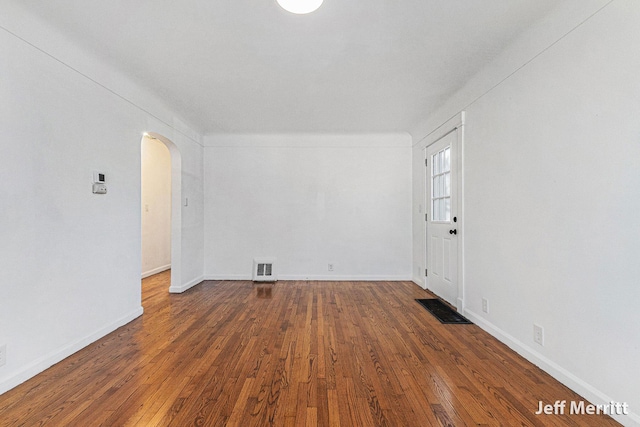 empty room featuring dark wood-type flooring, visible vents, arched walkways, and baseboards