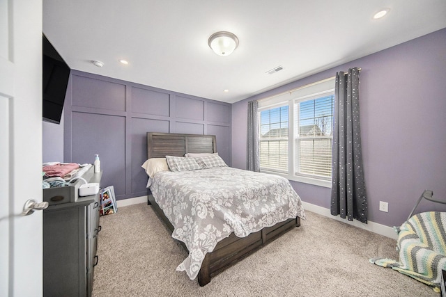 bedroom featuring visible vents, recessed lighting, a decorative wall, baseboards, and light colored carpet