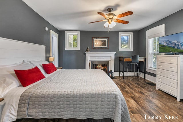 bedroom featuring baseboards, a glass covered fireplace, multiple windows, and dark wood finished floors
