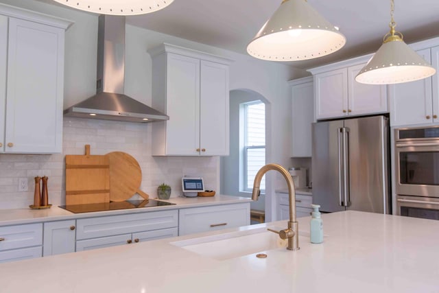 kitchen featuring tasteful backsplash, light countertops, stainless steel appliances, wall chimney exhaust hood, and a sink