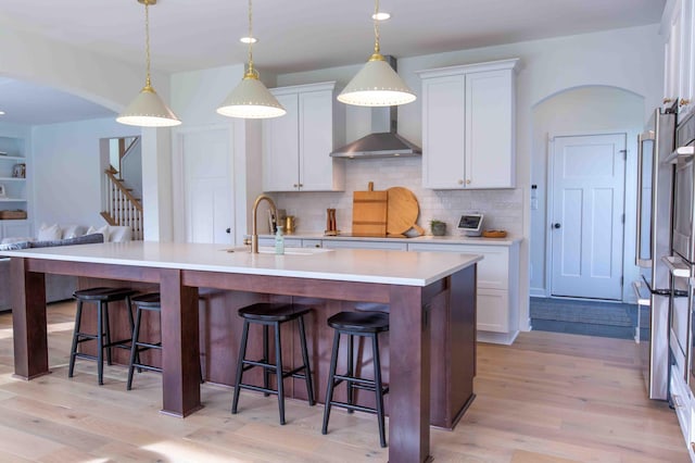 kitchen featuring arched walkways, a kitchen bar, wall chimney range hood, and a sink