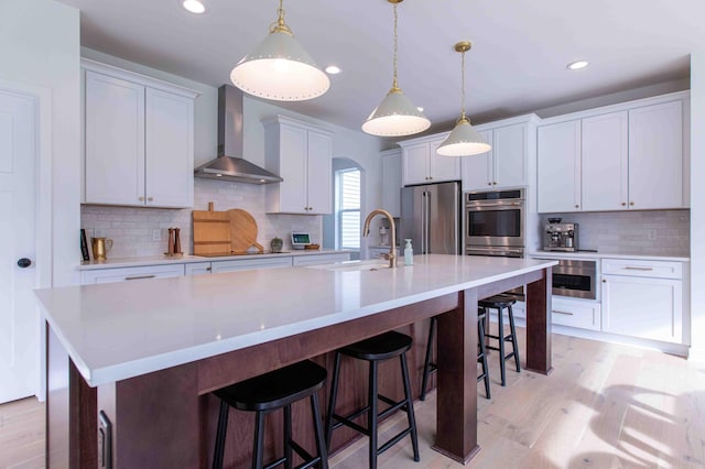 kitchen featuring a spacious island, light wood-style flooring, a sink, stainless steel appliances, and wall chimney exhaust hood