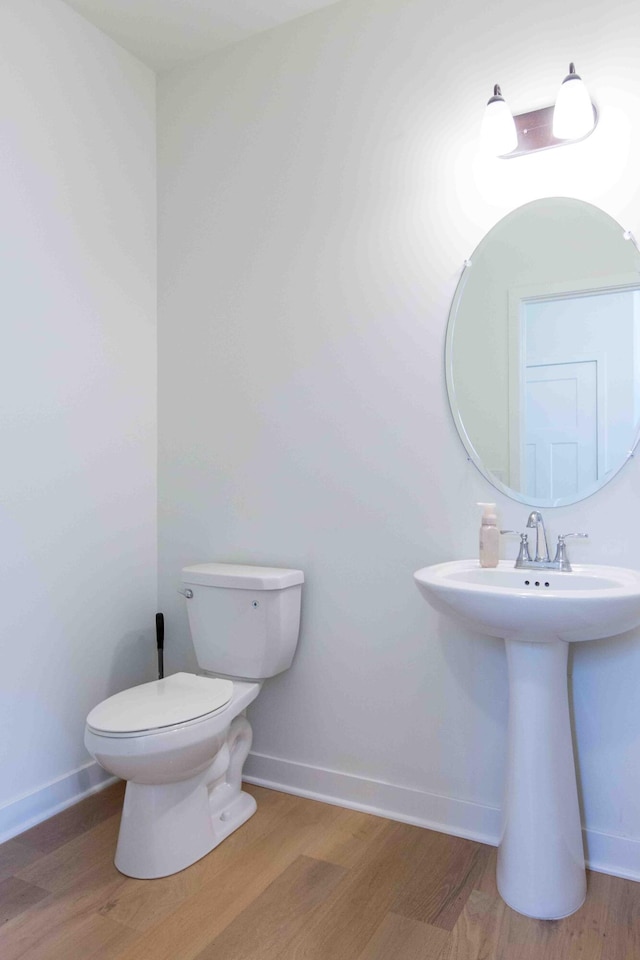 half bath with toilet, wood finished floors, and baseboards