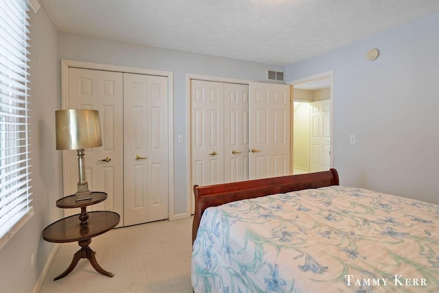 carpeted bedroom featuring visible vents, a textured ceiling, two closets, and baseboards