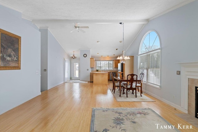 dining room with a tiled fireplace, crown molding, beamed ceiling, and light wood-style flooring