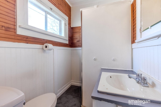 bathroom with a sink, toilet, wood walls, and wainscoting