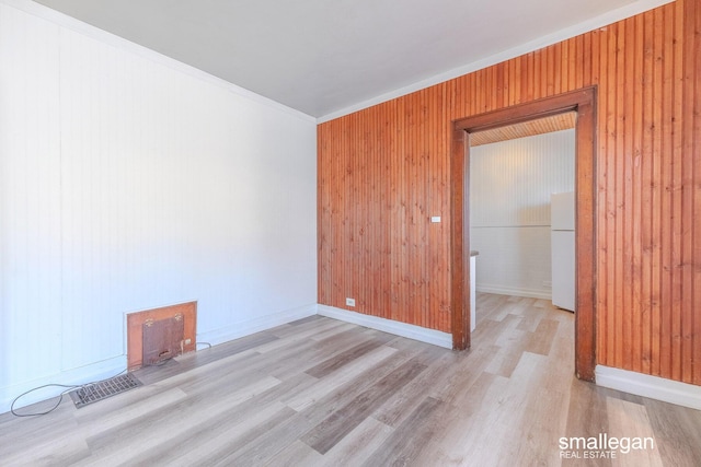 empty room featuring light wood-style flooring, visible vents, and wood walls